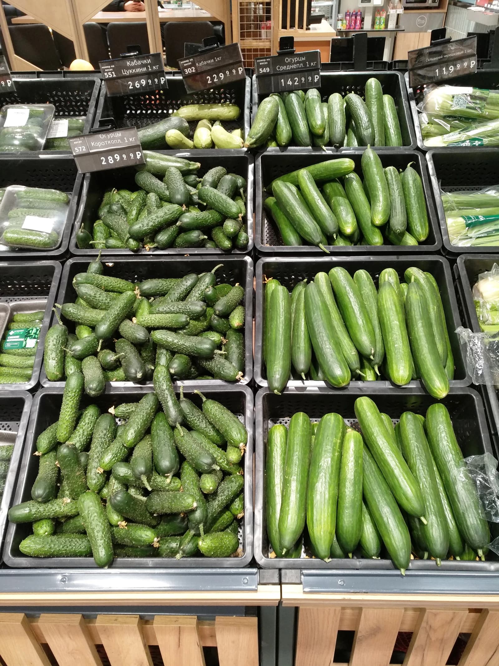 Various types of cucumbers displayed in black crates with price tags in a grocery store.
