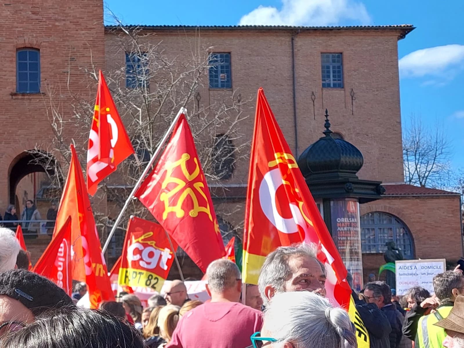 People gathered at a protest event with many red CGT union flags flying.