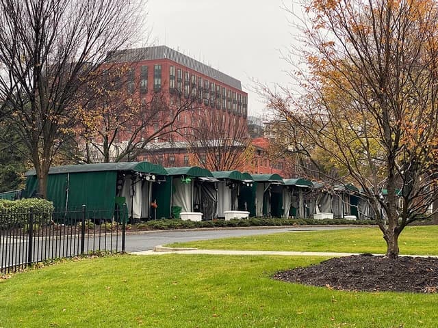 Temporary outdoor press stands with green canopies and white curtains set up outside the White House.