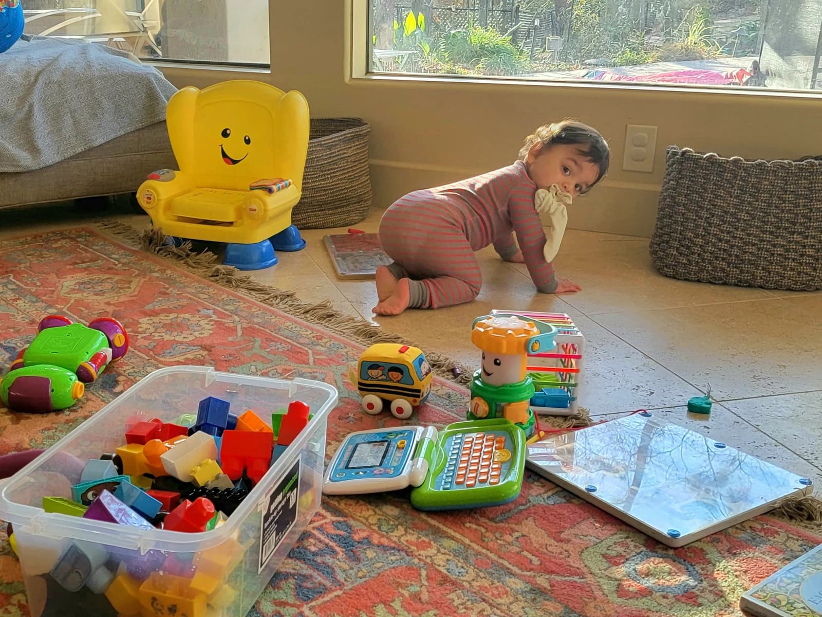 An American toddler plays on a colorful rug with building blocks and other toys.