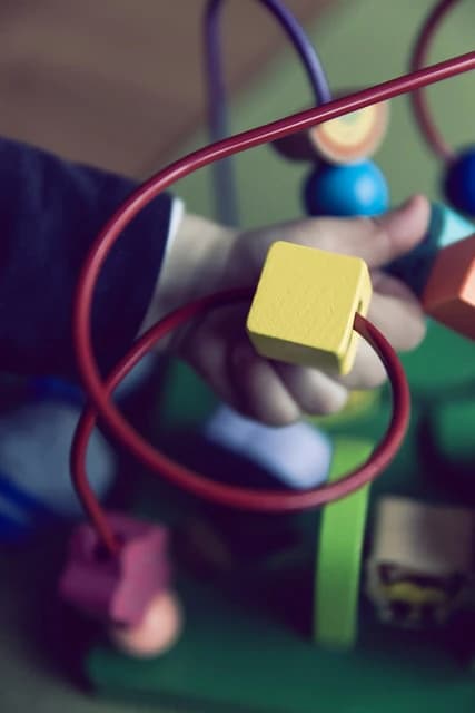 Toddler's hand manipulating a yellow block on a red wire bead maze toy.