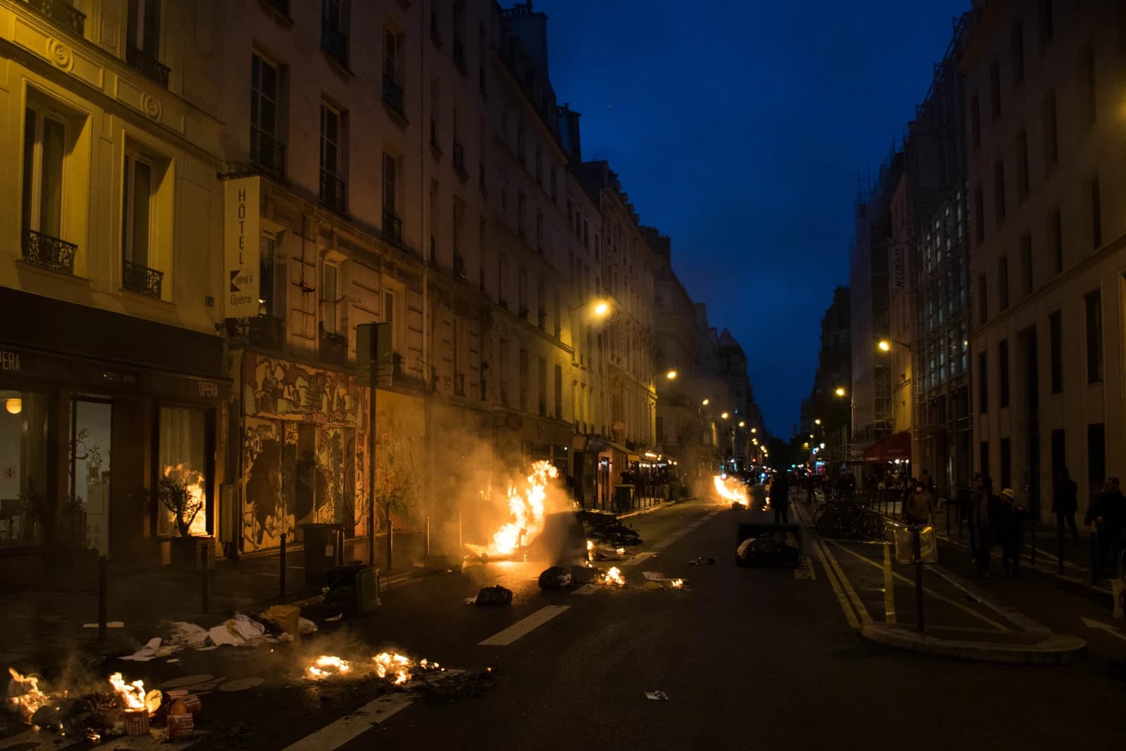 Fires burning on a street in Paris at night during a protest with buildings lining the street.