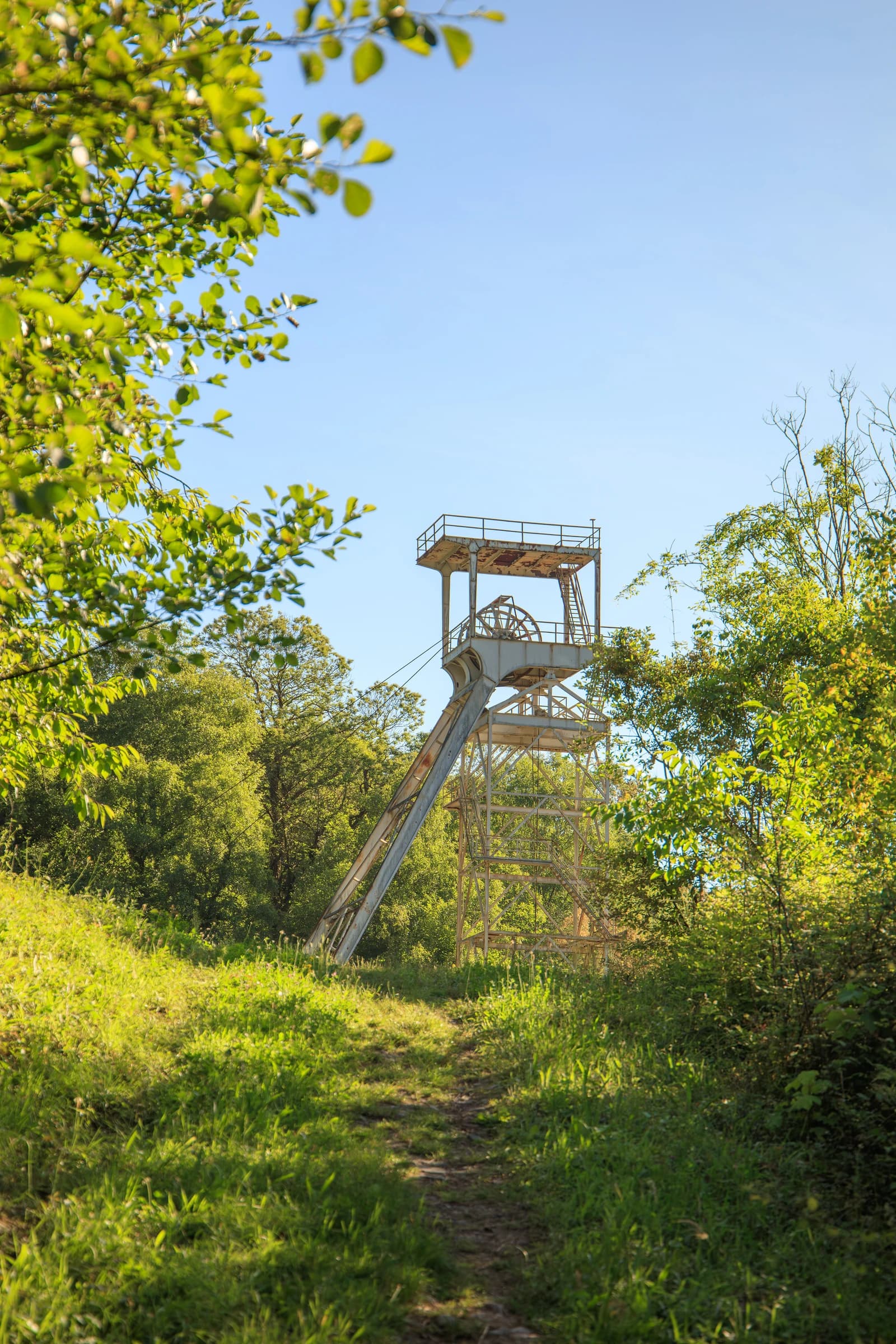 An old headframe of Pozu Tres Amigos coal mine surrounded by green trees.