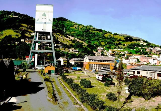 An overhead gantry of a mine shaft with buildings and green hills behind.