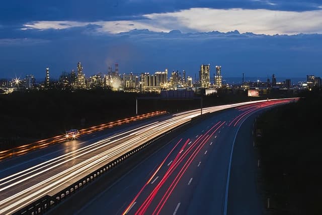 OMV refinery in Schwechat illuminated at night with light trails from passing cars on a highway.