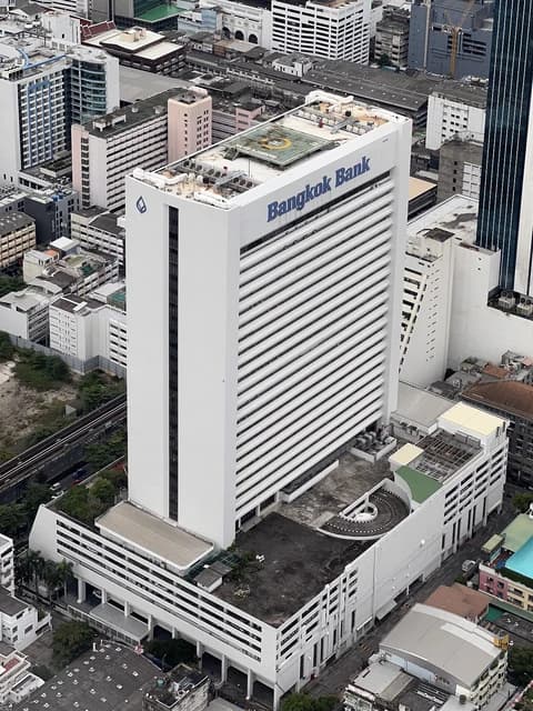 Aerial view of a white skyscraper, the Bangkok Bank, surrounded by other buildings.