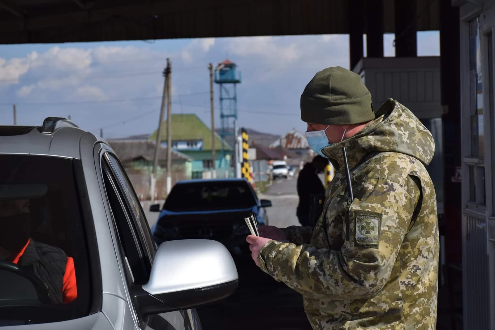 Ukrainian border guard in uniform and face mask checking documents at a border checkpoint.