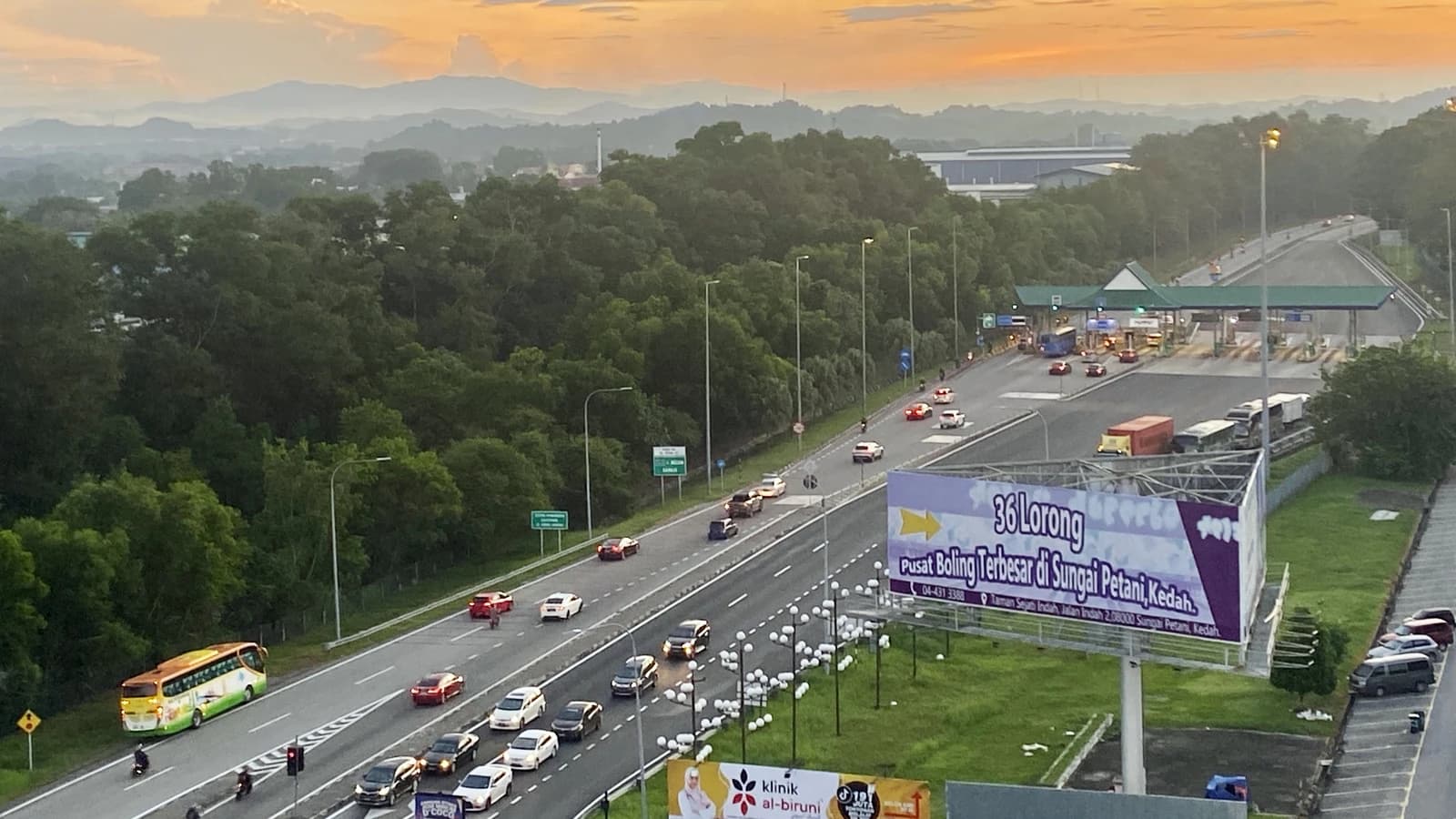 Cars and a bus on a multi-lane highway approaching a toll plaza at sunset.