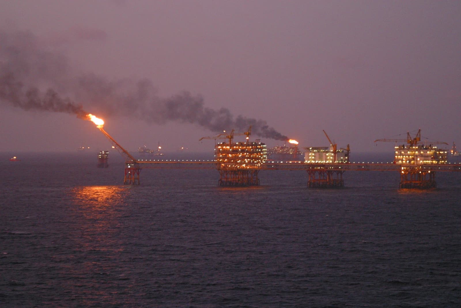 Oil rigs on the ocean with flames burning from stacks at dusk.