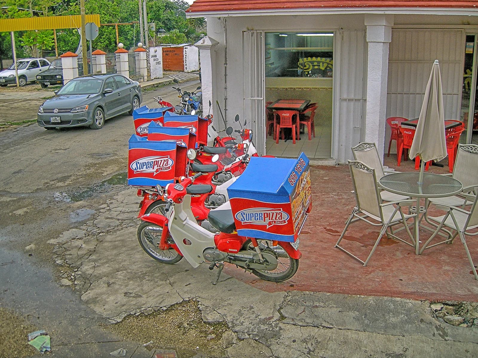 Delivery motorcycles with red and blue SuperPizza boxes parked outside a restaurant.