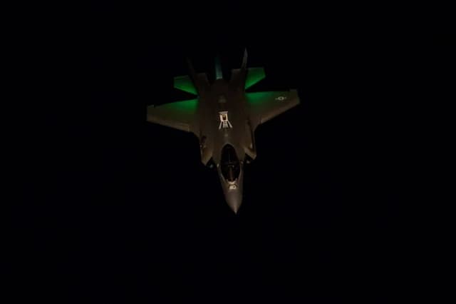 F-35 Lightning II fighter jet flying at night with green lights visible.