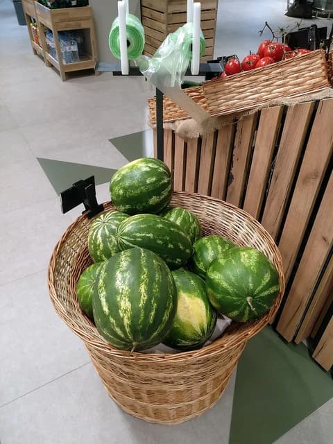 Watermelons displayed in a large woven basket inside a grocery store.