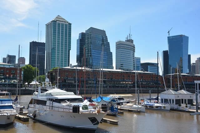 Boats docked at a marina with modern skyscrapers under a clear blue sky.