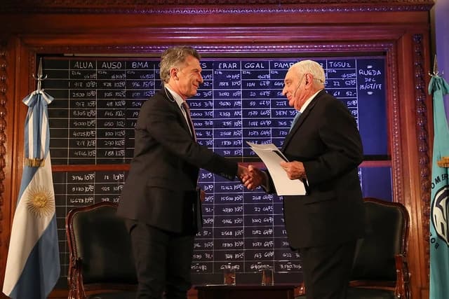 Mauricio Macri, former President of Argentina, shaking hands with another man indoors.