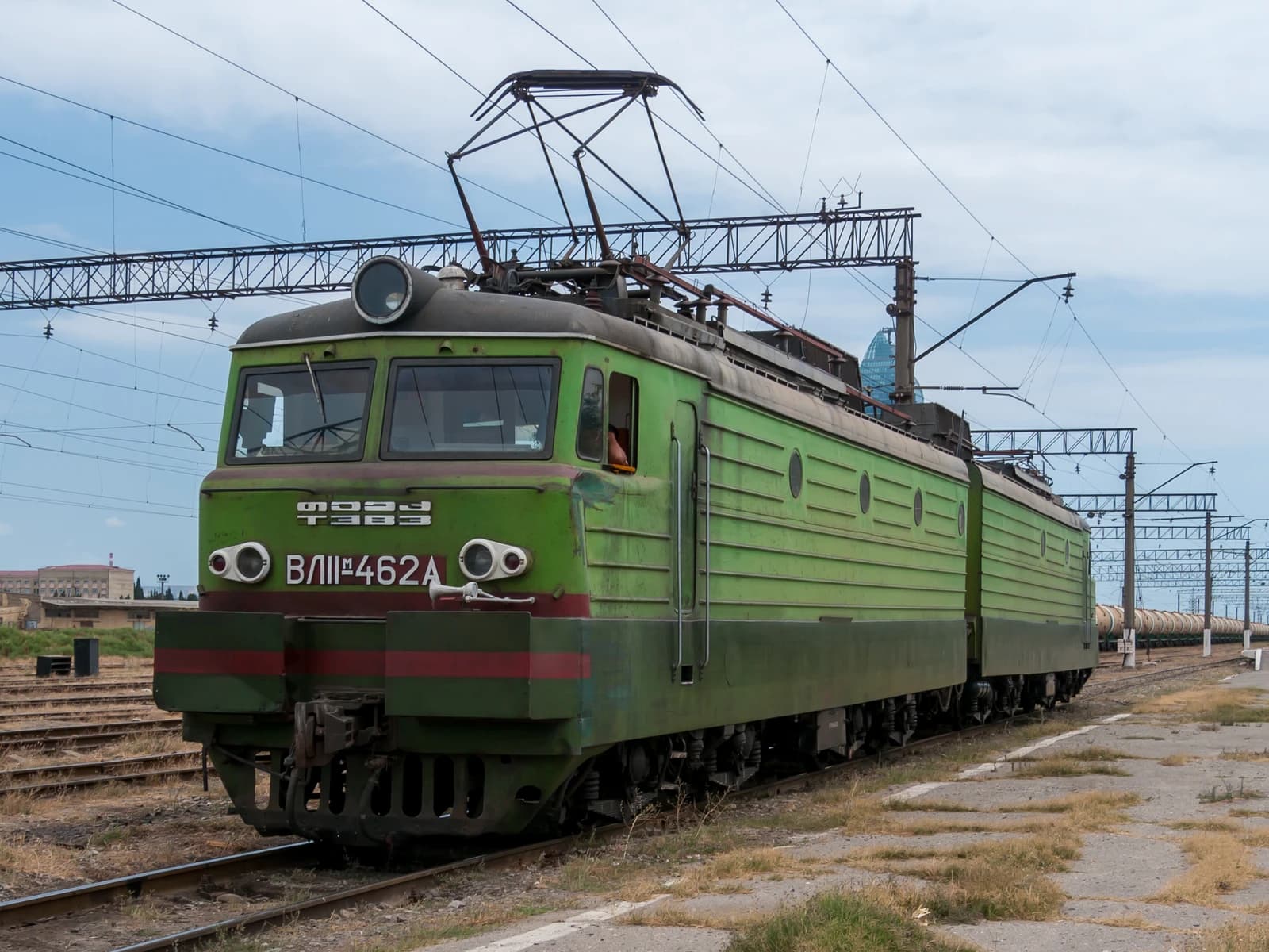 Green electric locomotive VLI-462A parked on train tracks in a rail yard.