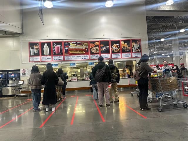 Shoppers waiting in line at a food court counter in a Costco store.