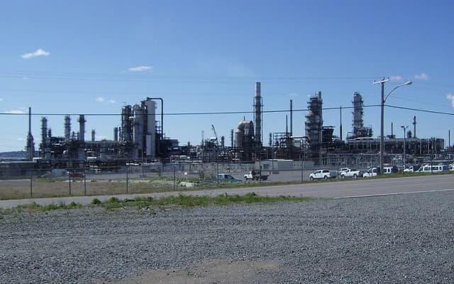 An industrial oil refinery with multiple processing towers and pipes under a bright blue sky.