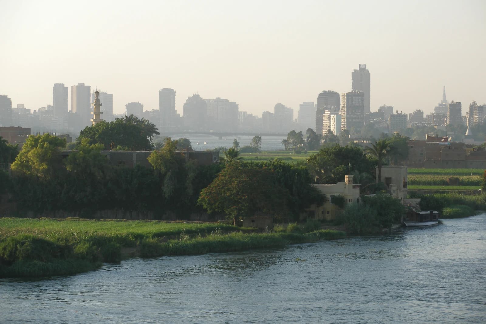 Cairo city skyline with modern buildings, a minaret, and the Nile River.