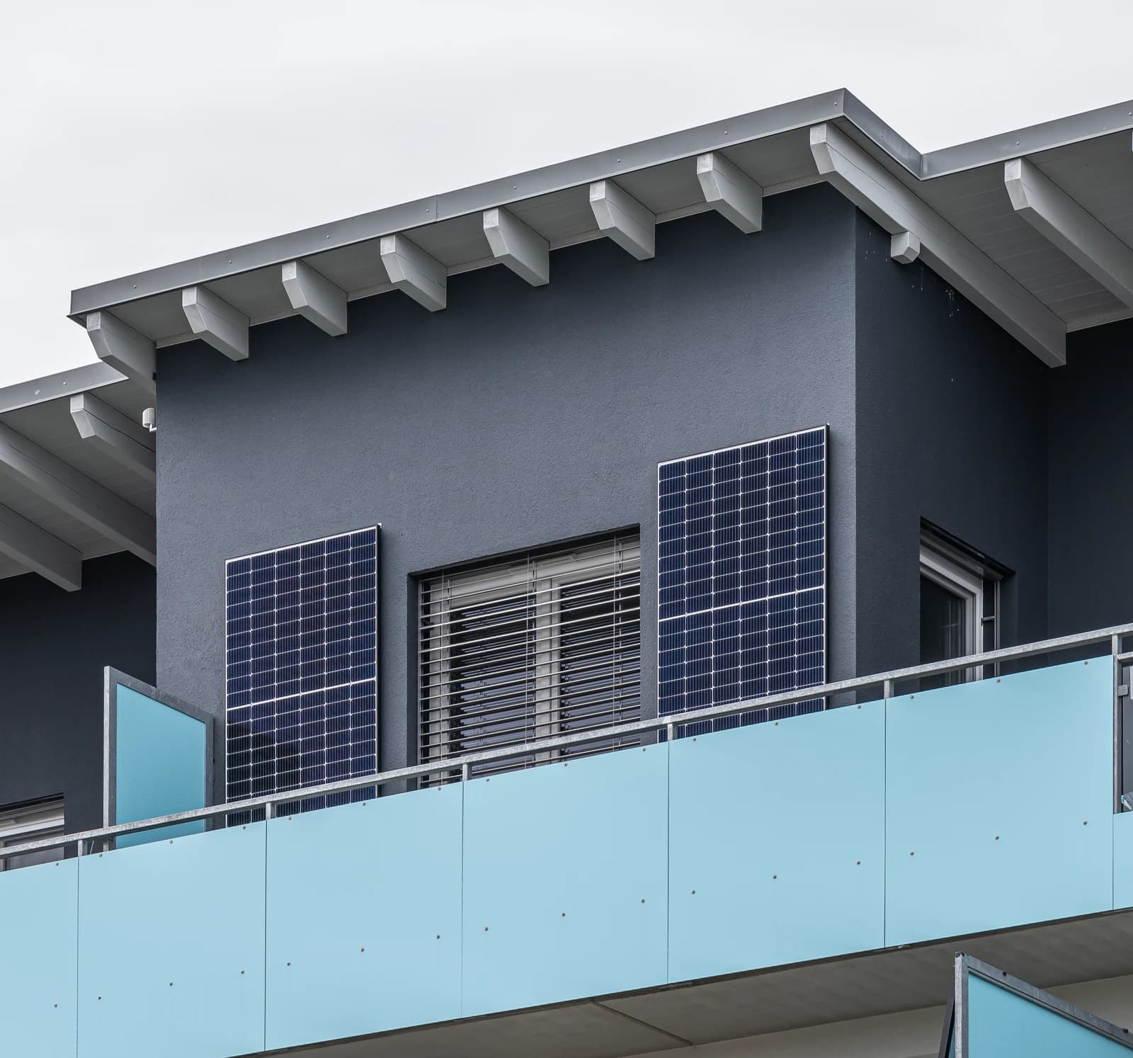 Two solar panels are installed on the wall of a balcony on a grey building.
