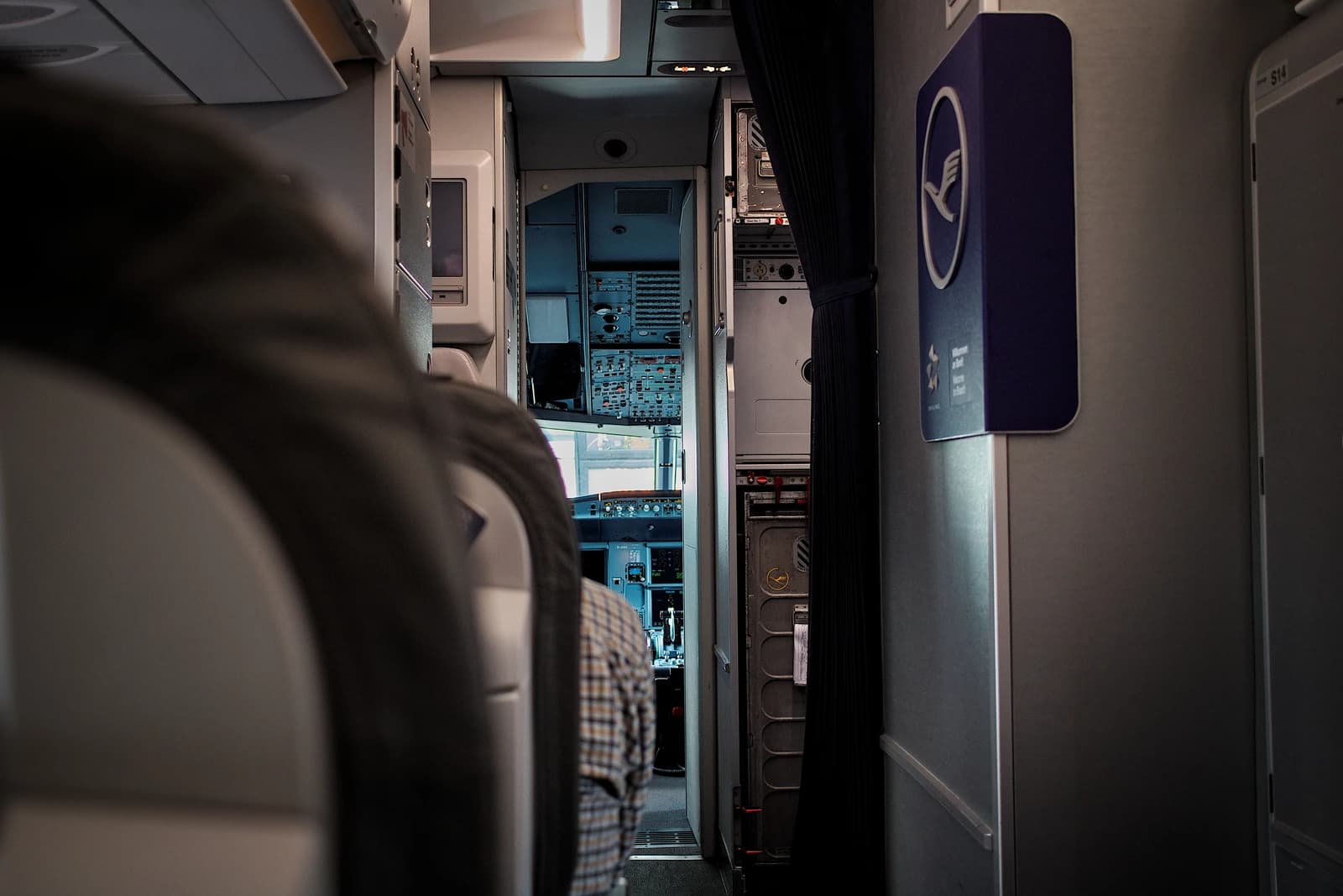 View from an airplane cabin into the cockpit with a pilot in a plaid shirt.