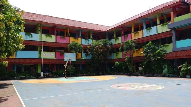 Exterior of SMPN 98 Jakarta school building with multiple colorful floors and a basketball court.