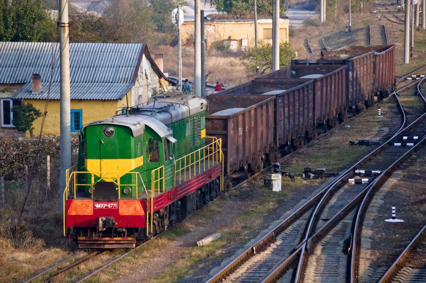 Green and yellow locomotive pulling a line of brown freight cars on railway tracks.