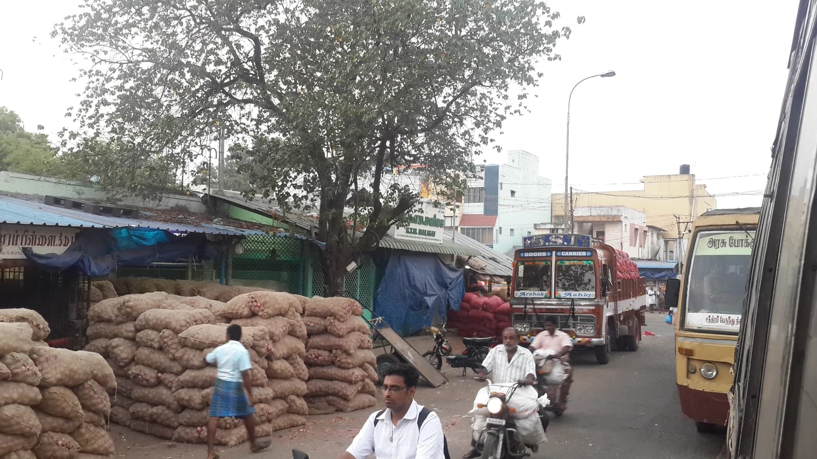 Sacks of onions piled high along a street in a bustling market area.