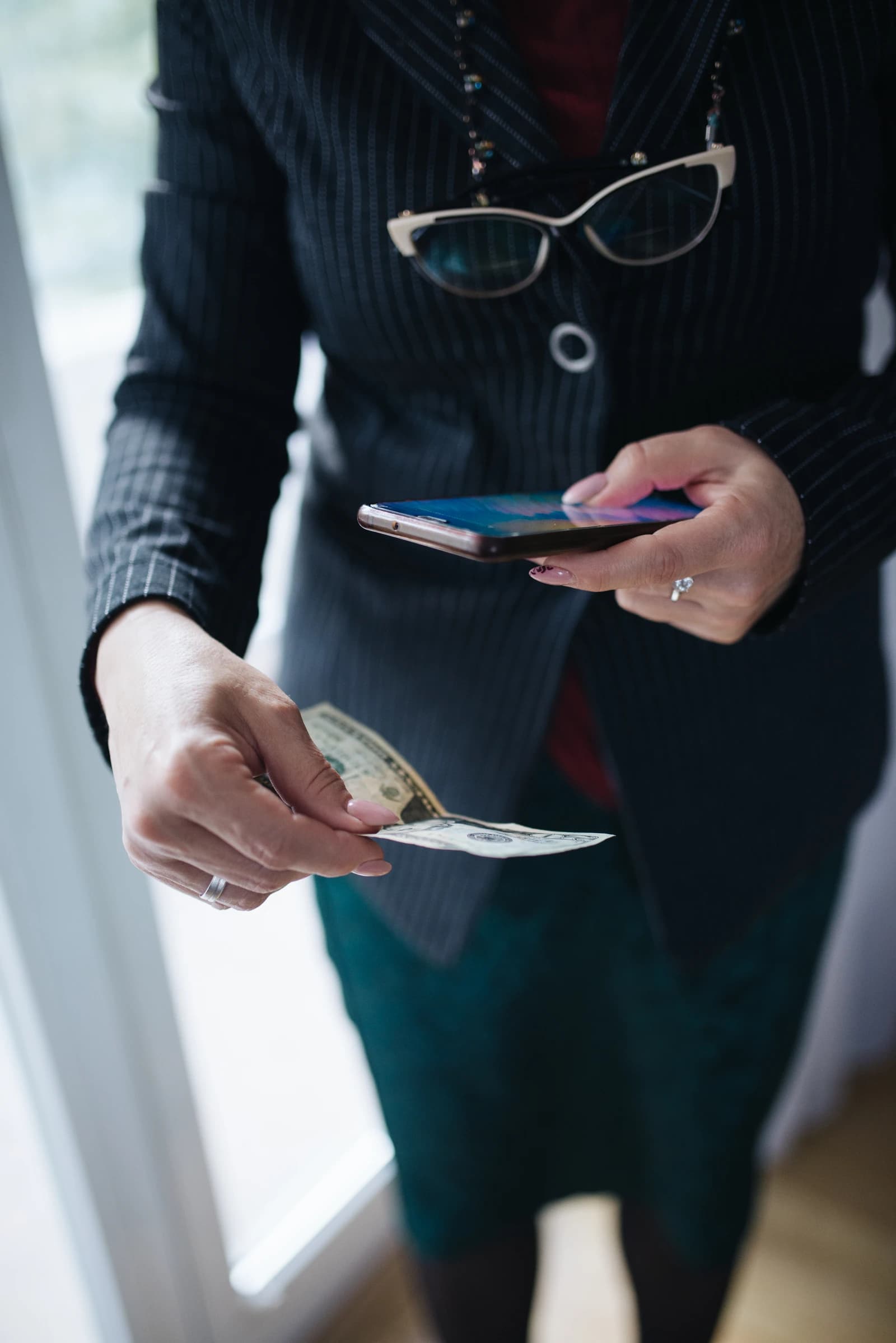 Businesswoman holding cash in one hand and a smartphone in the other.