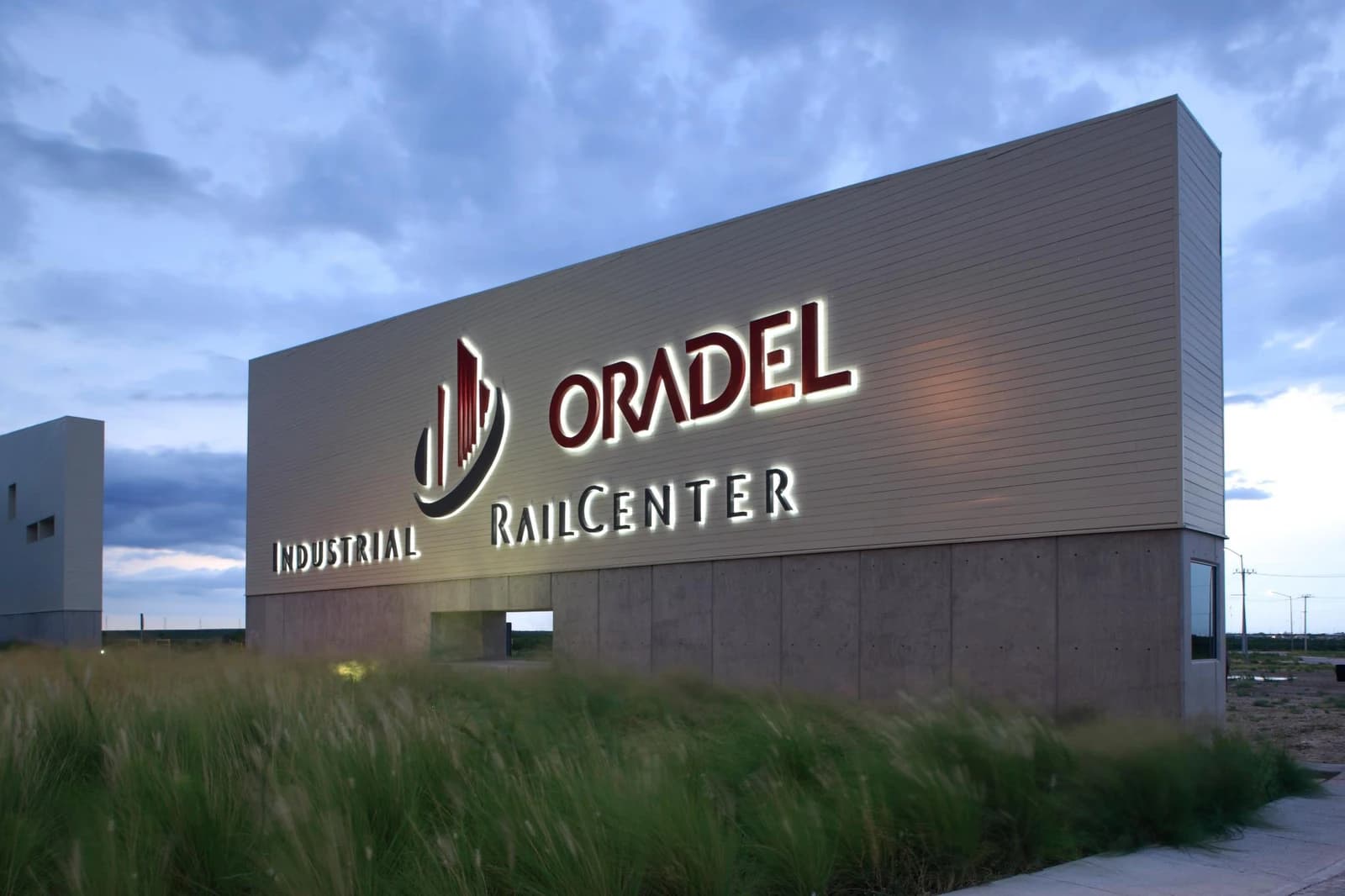 Entrance sign with 'Oradel Industrial RailCenter' illuminated, surrounded by tall grass.
