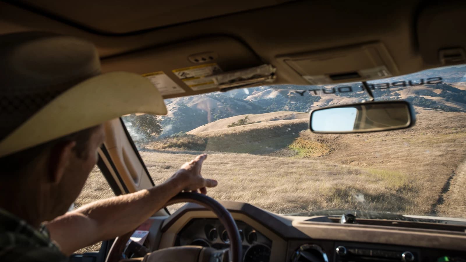 Rancher Ned Wood driving a vehicle and pointing to the dry landscape outside.