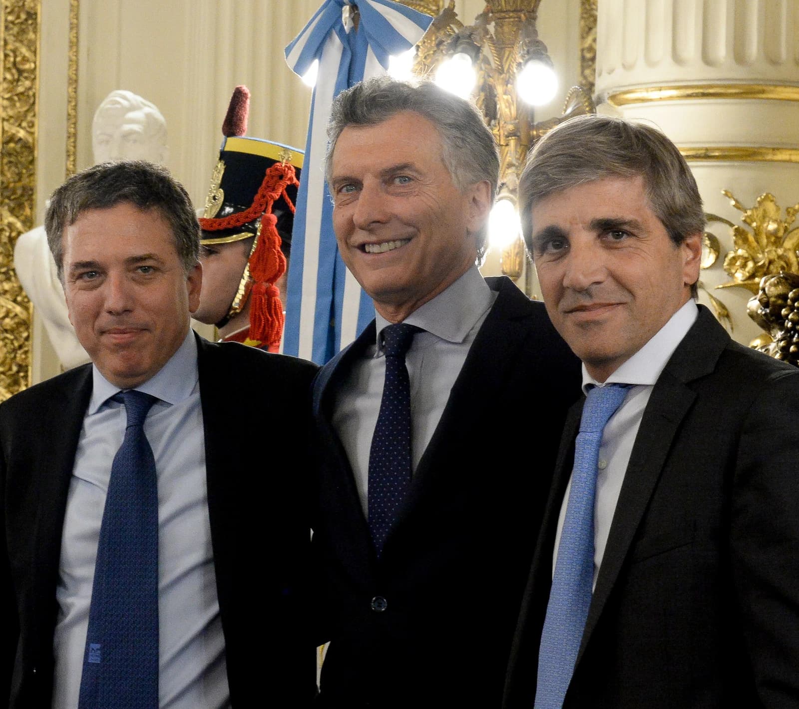 Nicolás Dujovne, Luis Caputo, and Mauricio Macri standing together in a formal indoor setting.