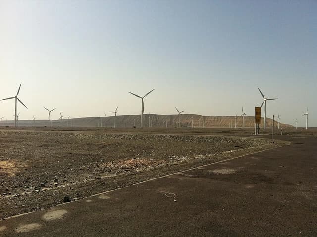 Wind turbines visible from a highway in a dry, mountainous region of Xinjiang, China.