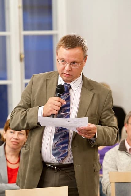 Raul Eamets, an Estonian academic, speaking at an event holding a microphone and notes.