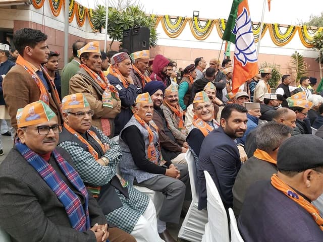 People attending an event, many wearing orange hats and scarves with BJP symbols.