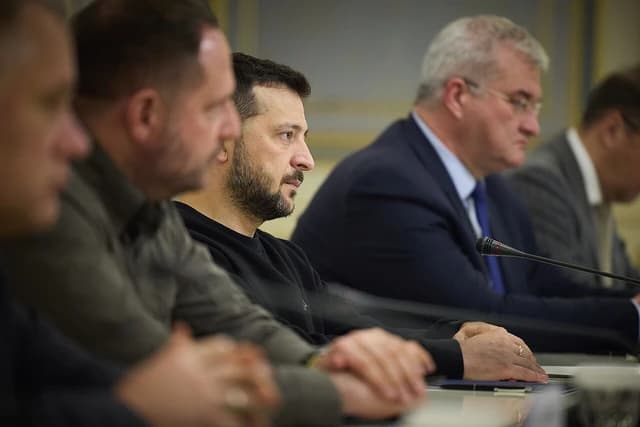 Volodymyr Zelenskyy, President of Ukraine, sitting at a conference table with other officials.