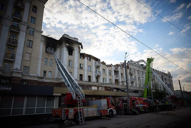 Damaged building in Dnipro with an extended ladder from a fire truck reaching a burned window.