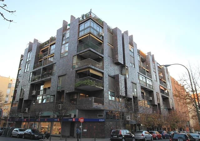 Modern apartment building exterior with balconies and street-level shops in Madrid.