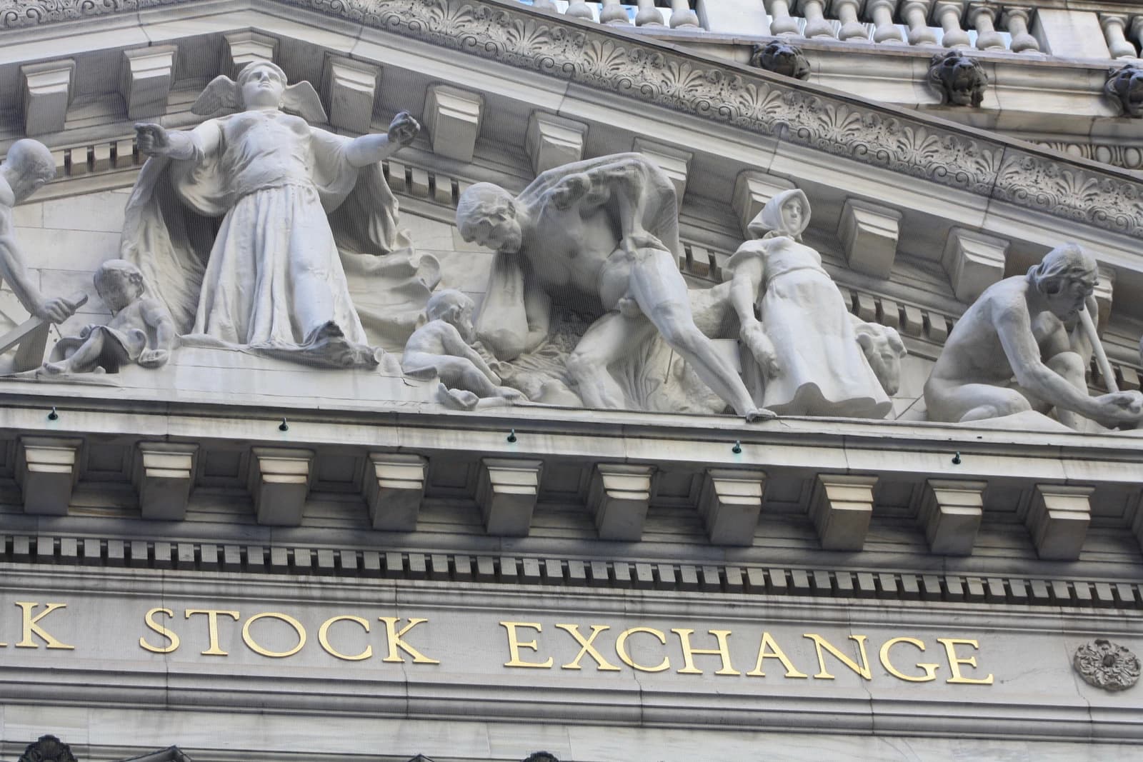 Close-up of the facade of the New York Stock Exchange building with sculptures and gold lettering.