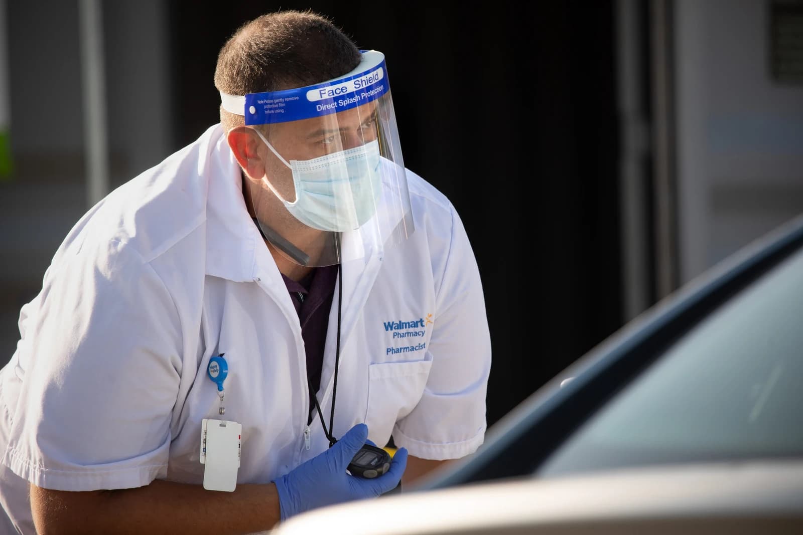 Walmart pharmacist wearing face shield and mask, leaning into a car window.