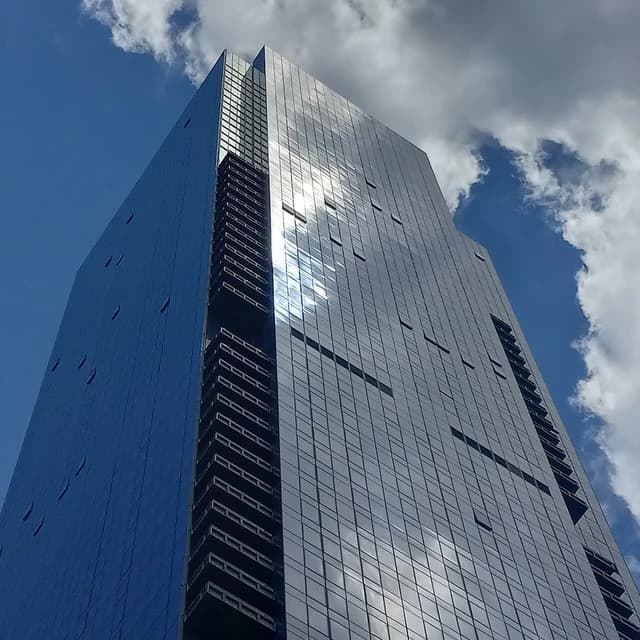 A modern glass skyscraper, Skyline Tower, reaching into a blue sky with clouds.