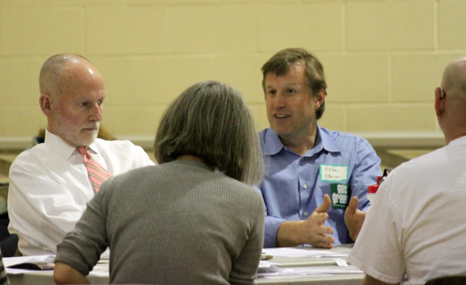 Man wearing name tag 'Mike O'Brien' speaks to others at a table.