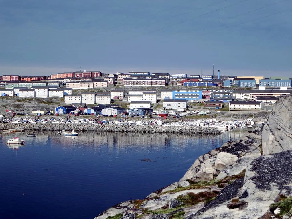 Colorful buildings and houses line a rocky coastline with boats docked in a harbor in Nuuk, Greenland.