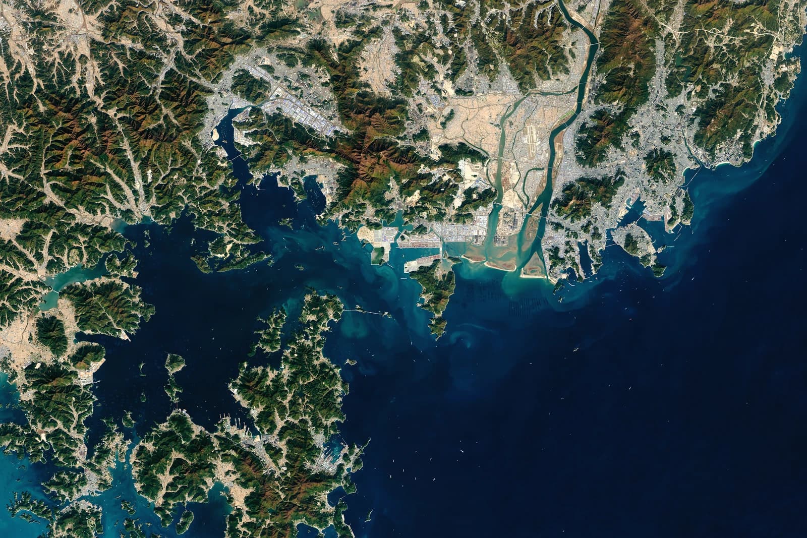 Satellite view of Port Busan, South Korea, with ships in the water and coastal cities.