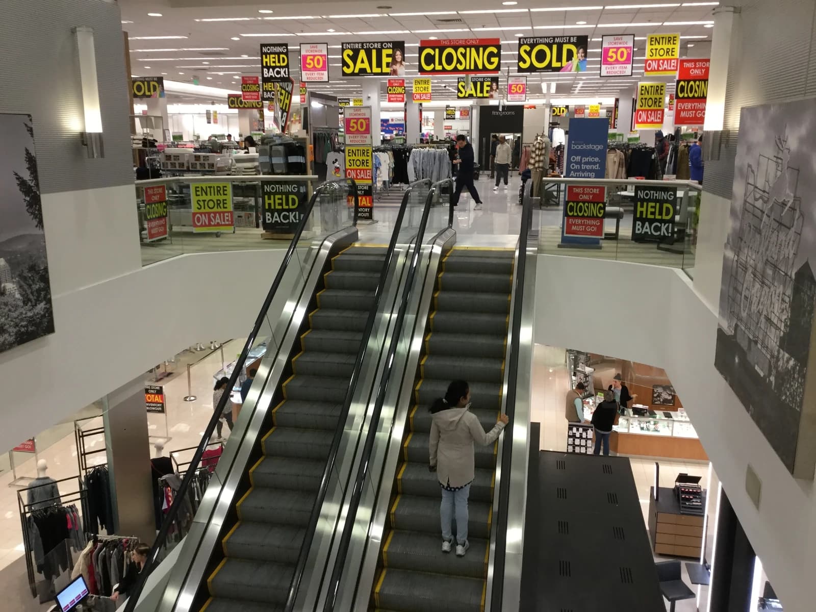 Interior view of Macy's department store with 'closing sale' banners displayed.