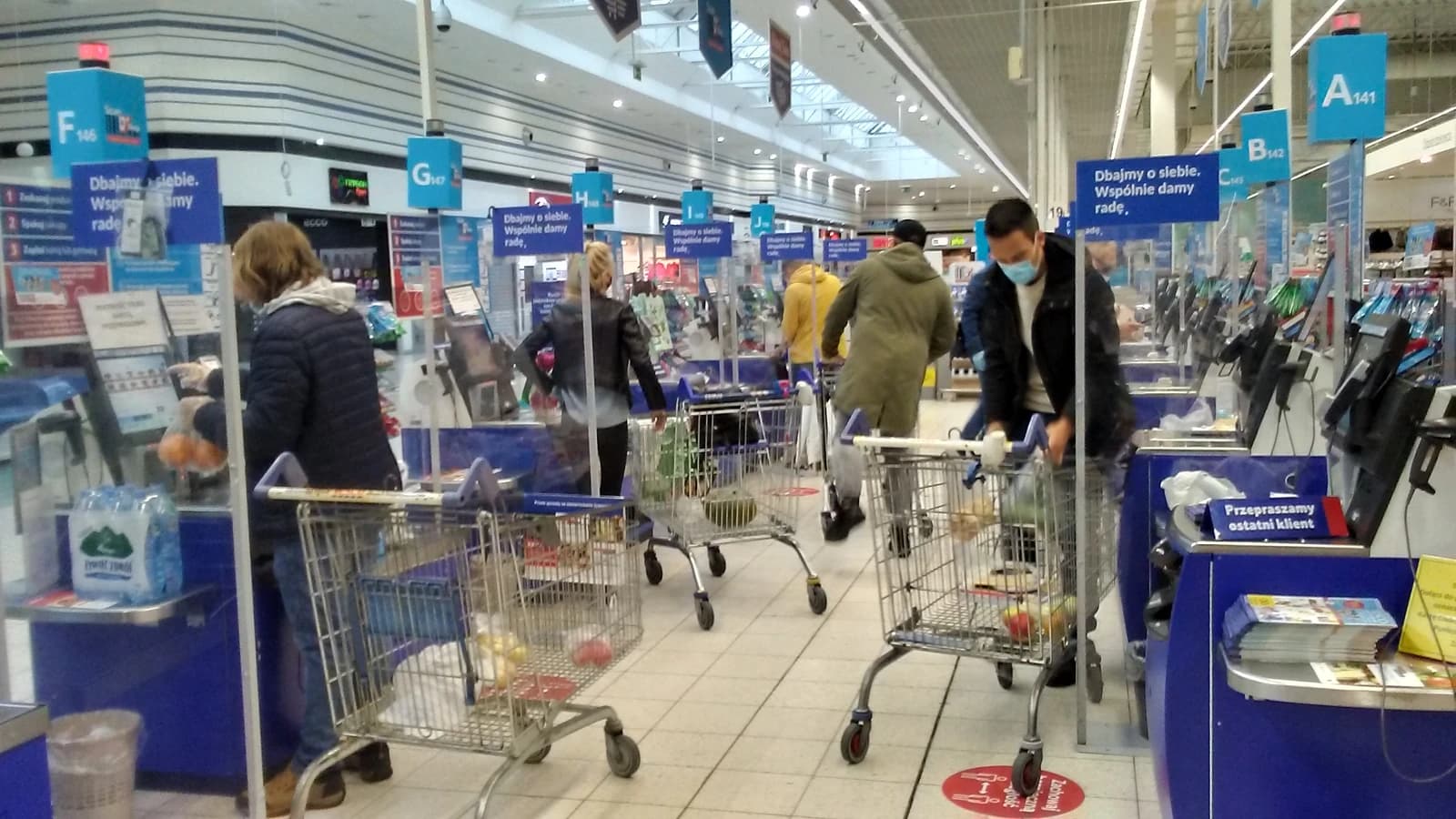 People with shopping carts using self-checkout machines inside a grocery store.