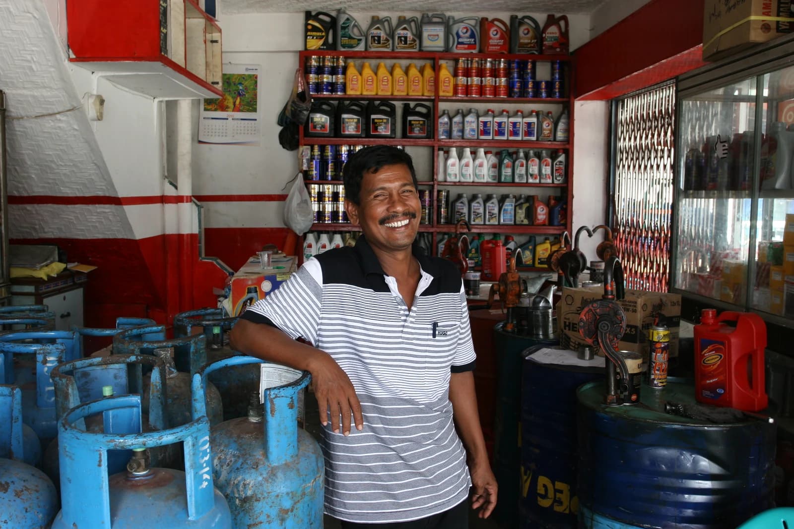 Smiling store owner in a striped shirt stands in his auto-garage shop.