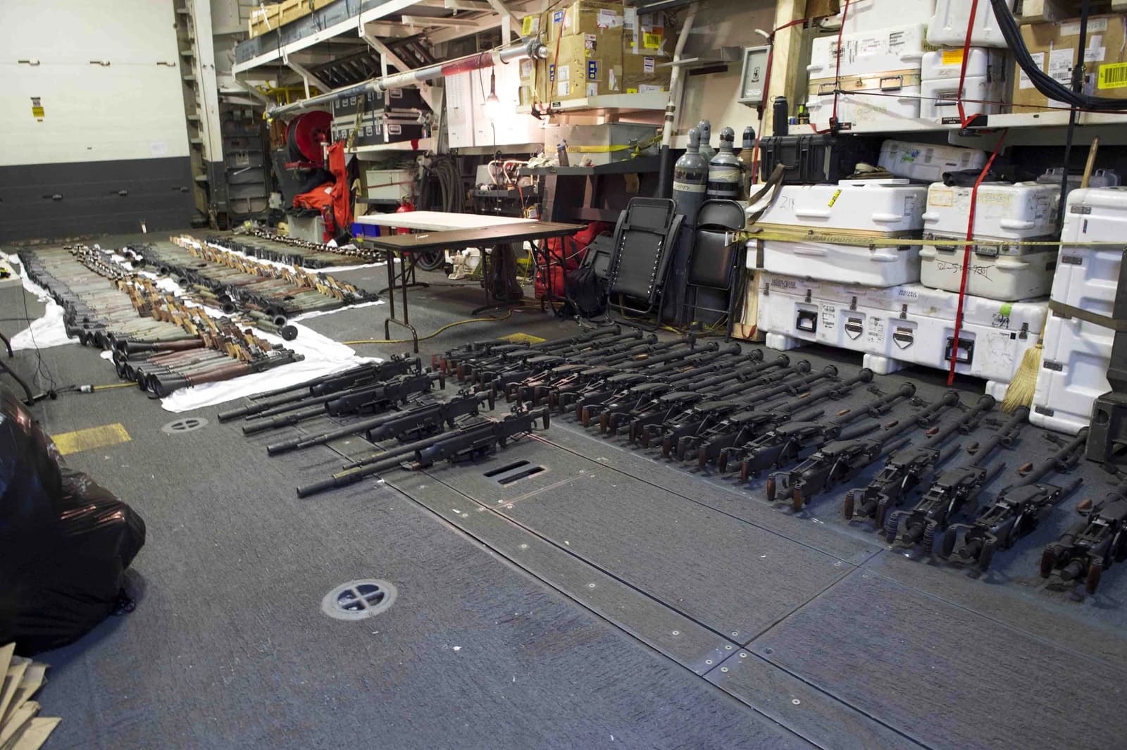 Numerous military-grade weapons, including rifles and rocket launchers, are laid out on a ship's deck.