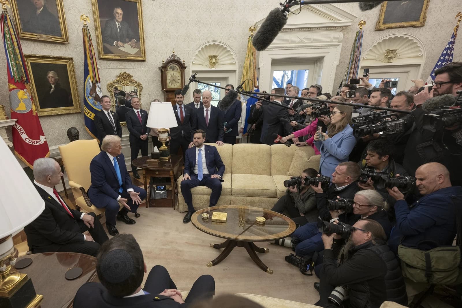 Donald Trump and Benjamin Netanyahu seated in conversation with media gathered around in the White House.