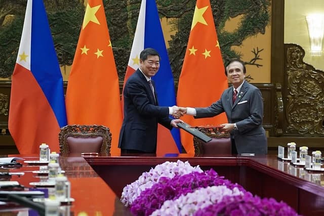 Officials from the Philippines and China shaking hands across a table with national flags behind them.