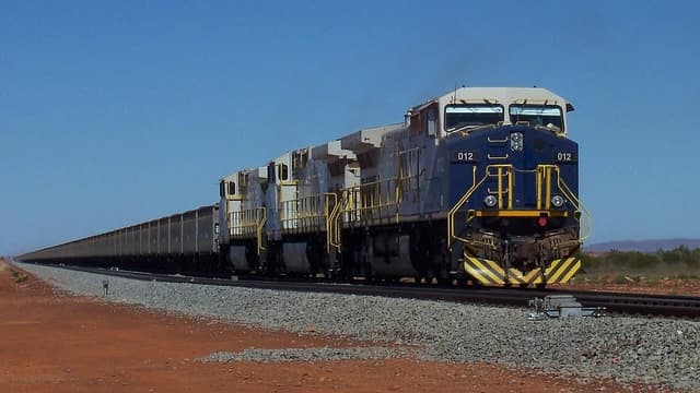 FMG locomotive 012 pulls a very long train of iron ore cars on a single track.